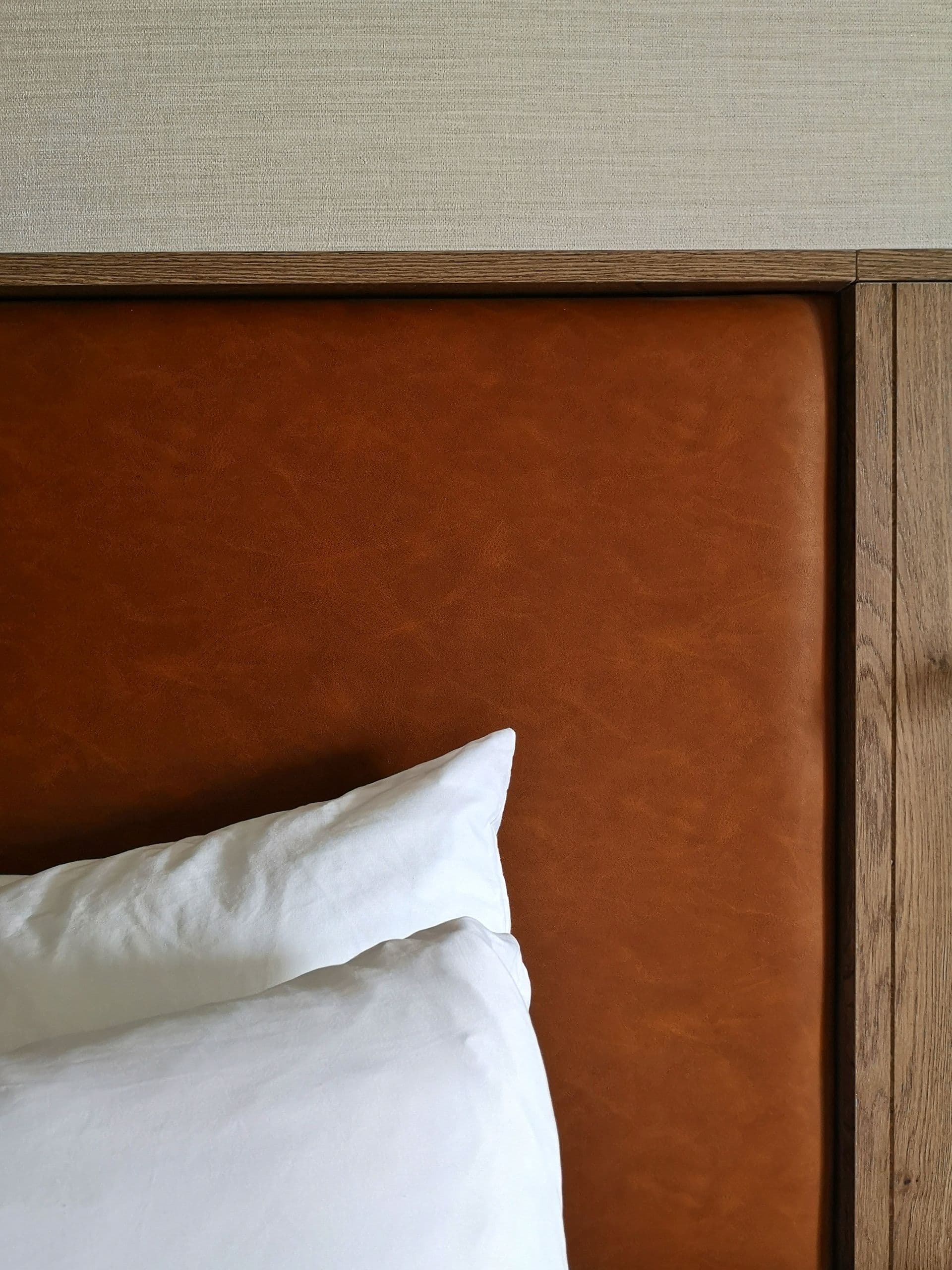 Warm bedroom detail with a leather headboard and crisp white bed linen