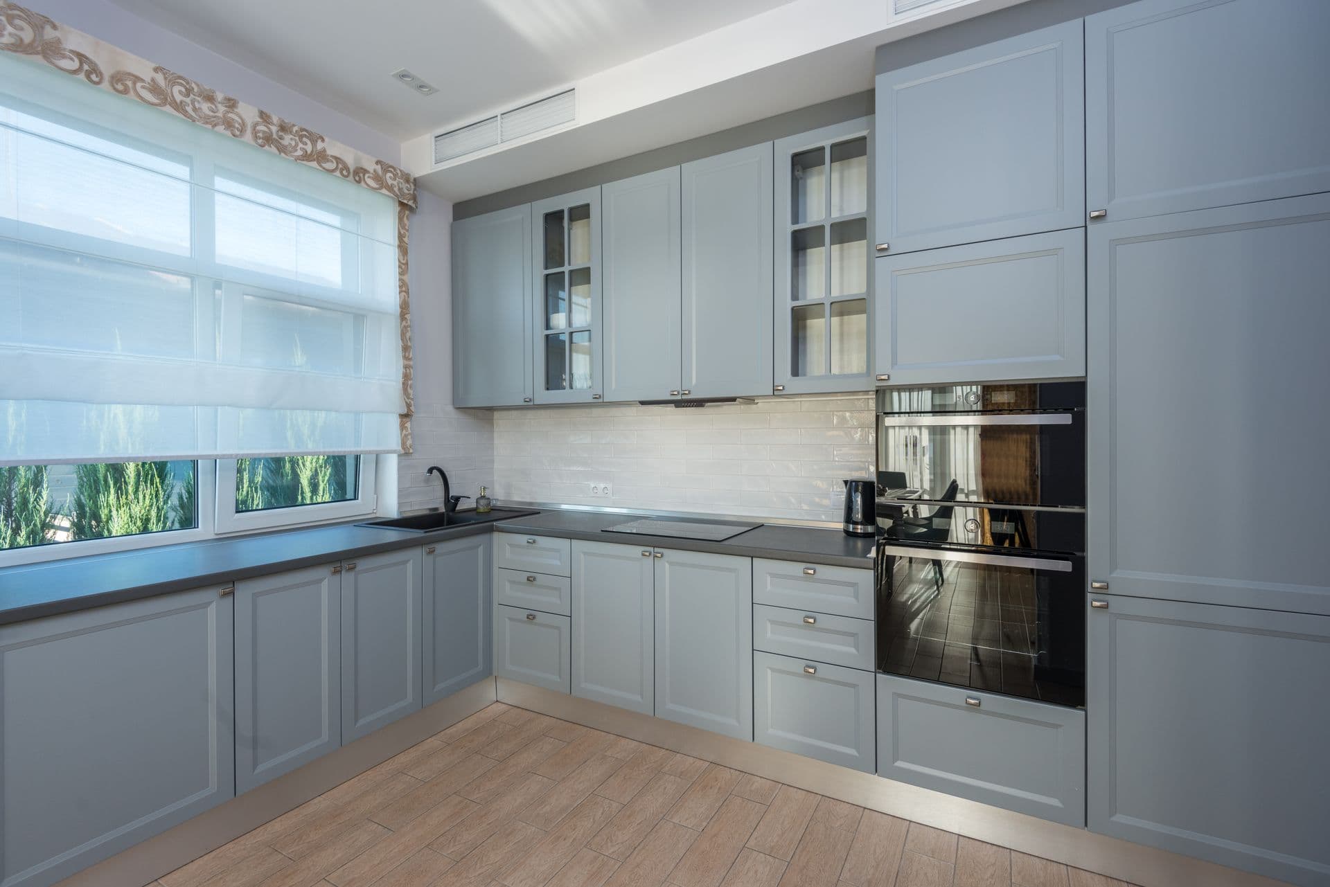 Bright kitchen with soft blue-grey cabinetry and a window overlooking greenery